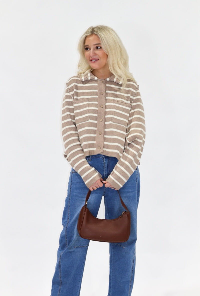 Woman wearing a striped sweater and blue jeans, holding a brown handbag on a white background