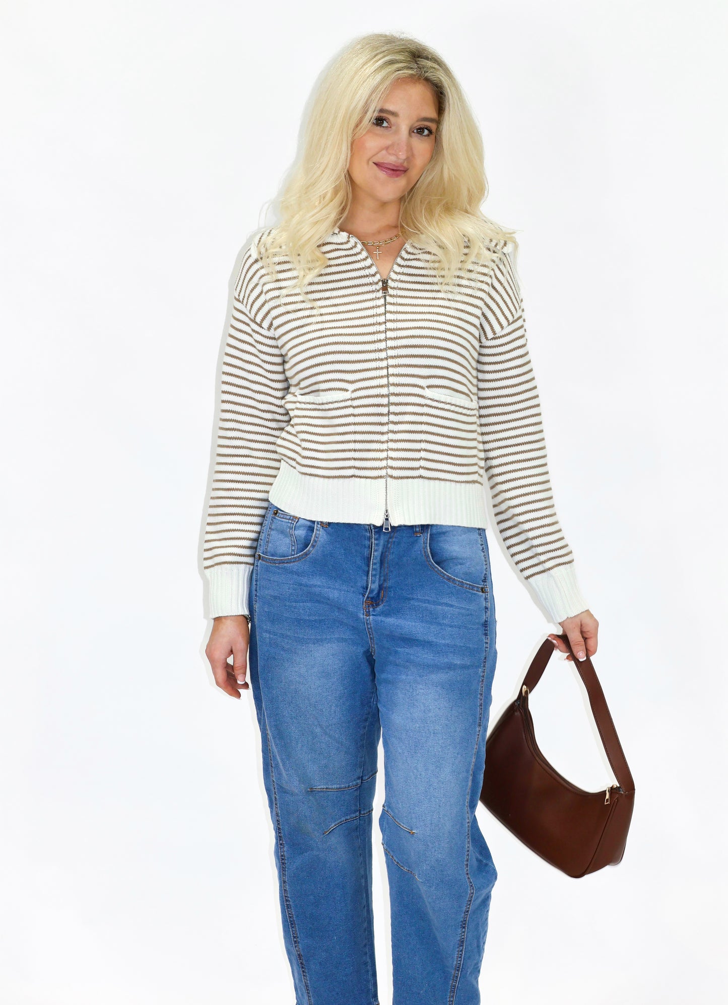 Woman wearing a striped shirt and blue jeans, holding a brown handbag on a white background