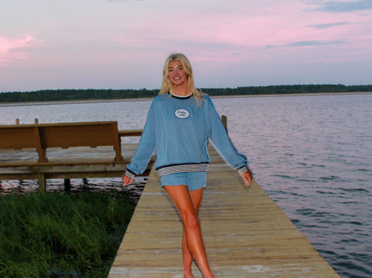 Woman in a blue outfit standing on a wooden dock by a lake at sunset.