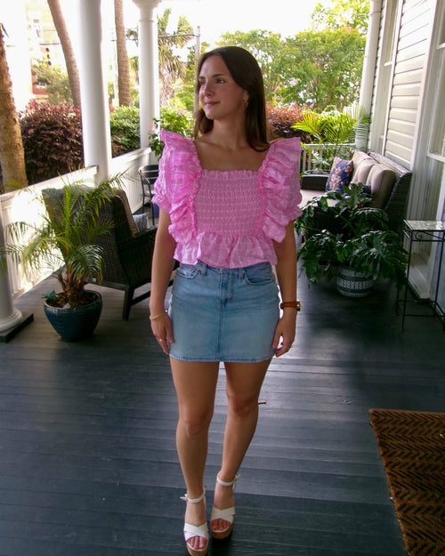 Woman wearing a pink top and denim shorts on a porch