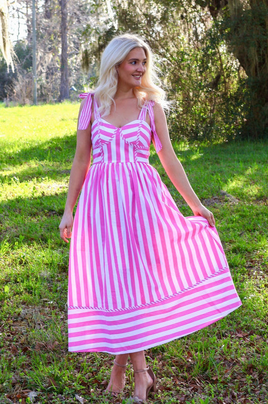 Woman wearing a pink and white striped dress in a grassy outdoor setting
