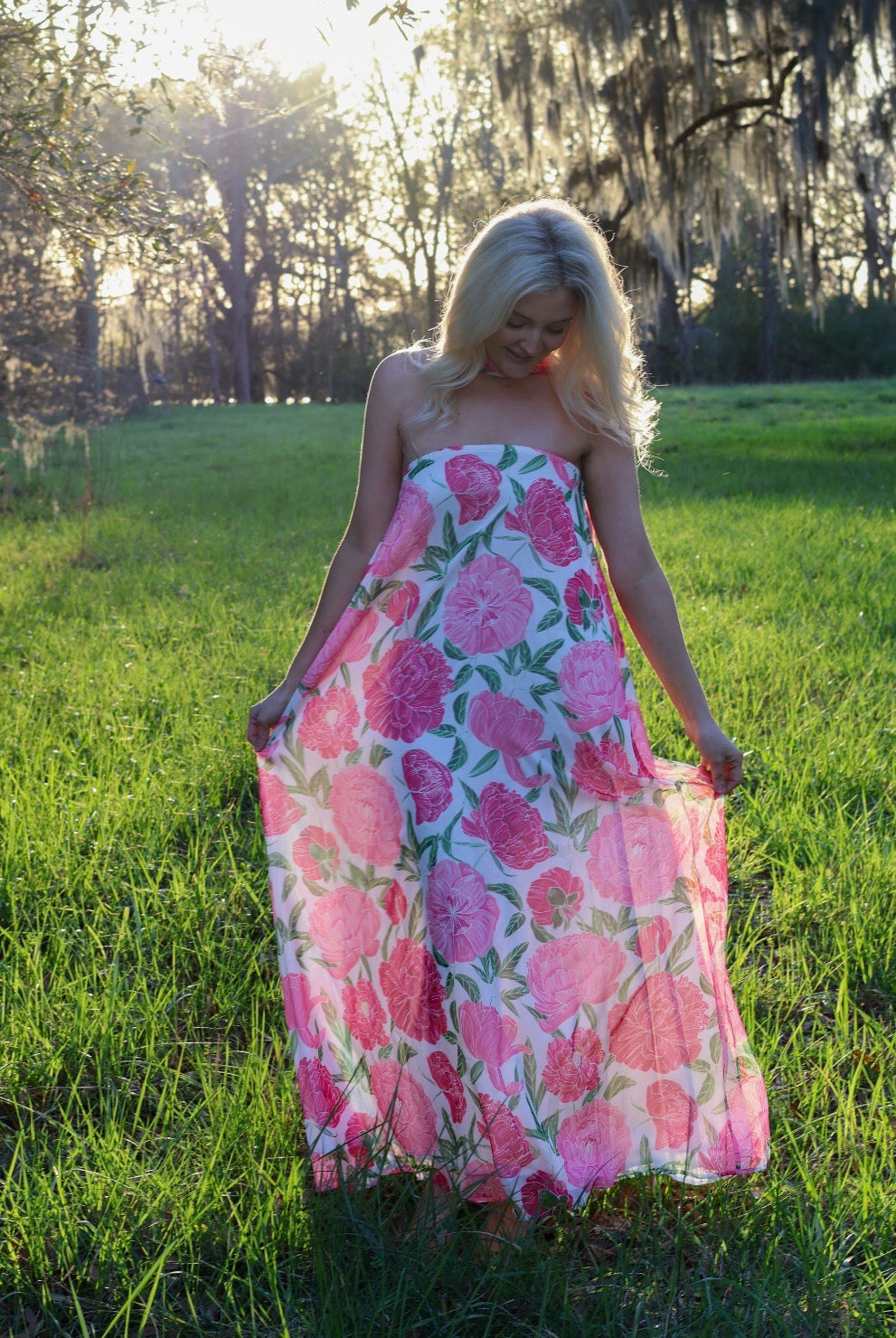 Woman in a floral dress standing in a grassy field with trees in the background