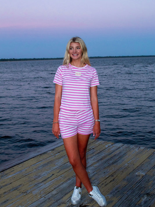 Woman in a pink and white striped dress standing on a dock by a body of water.