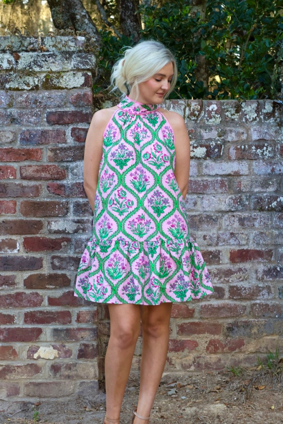 Woman wearing a patterned dress standing against a brick wall.