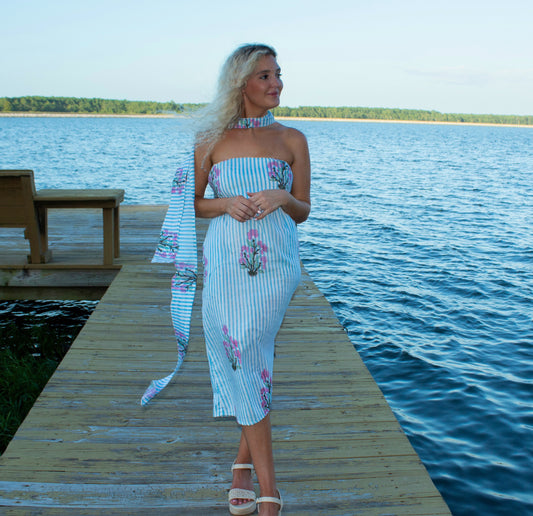 Woman in a strapless dress with floral patterns standing on a wooden dock by a lake.