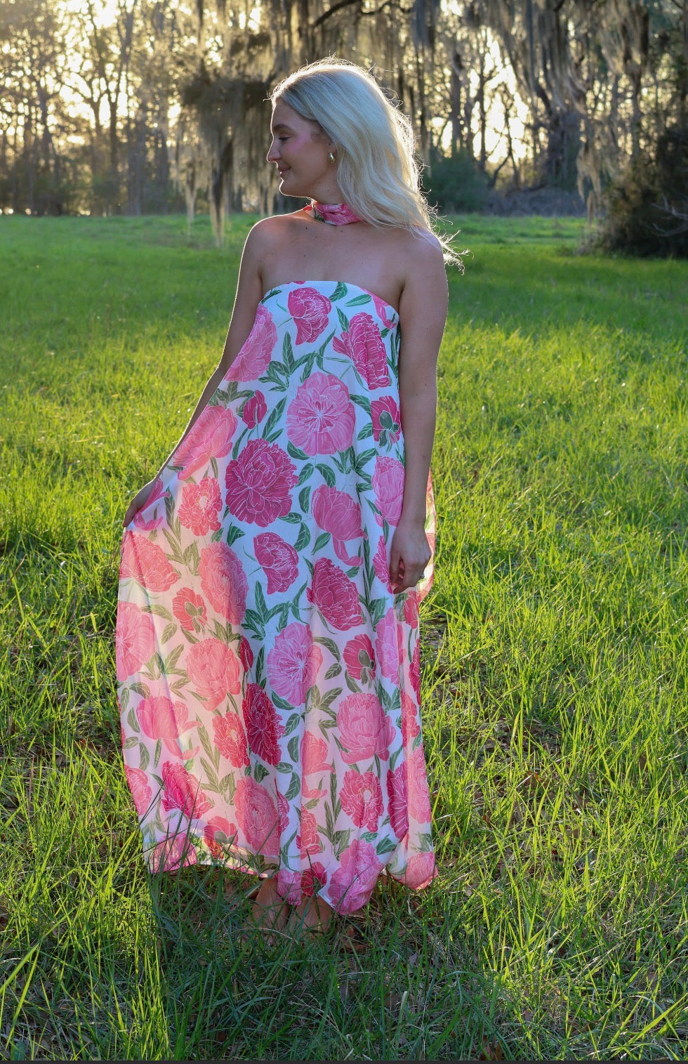 Woman wearing a pink floral dress standing in a grassy field.