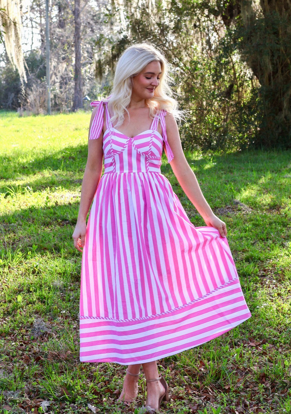 Woman wearing a pink and white striped dress standing in a grassy outdoor setting.