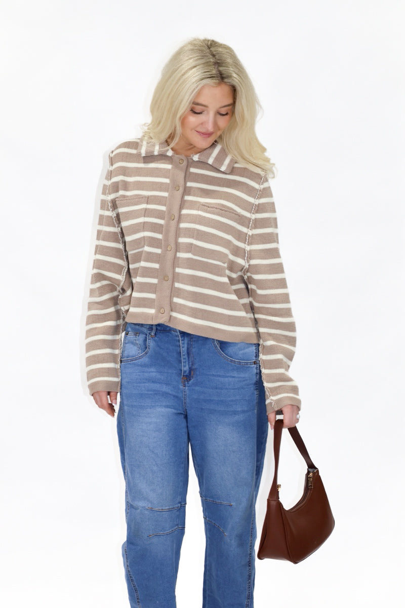 Woman wearing a striped sweater and blue jeans, holding a brown handbag on a white background