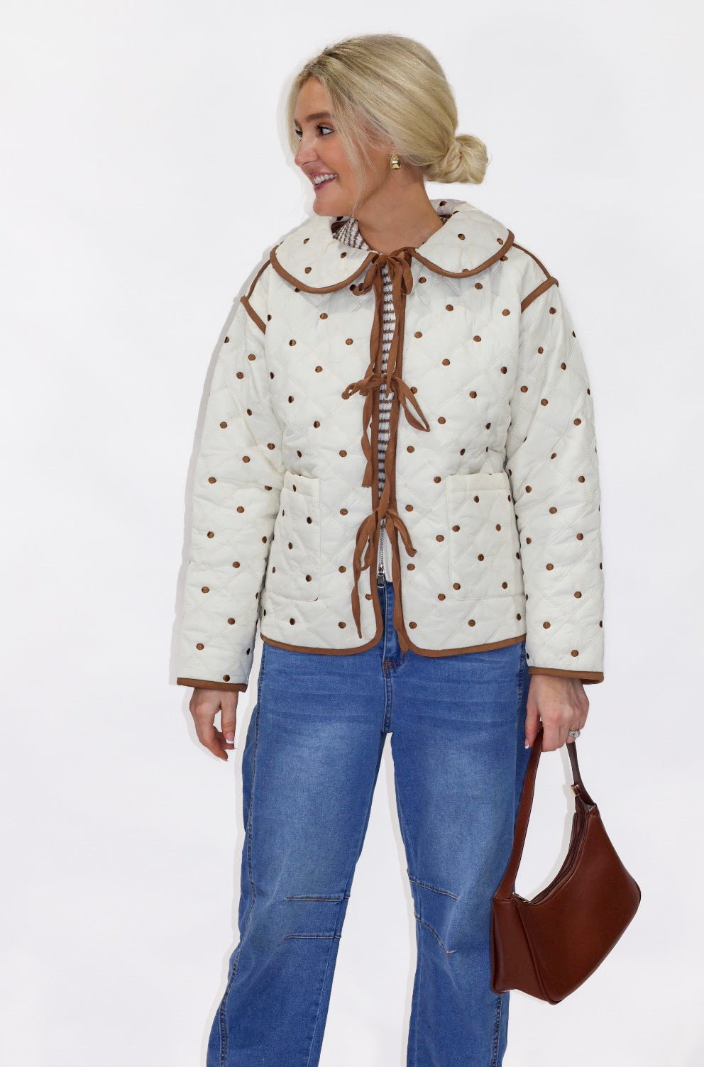 Woman wearing a cream quilted jacket with brown accents and blue jeans on a white background