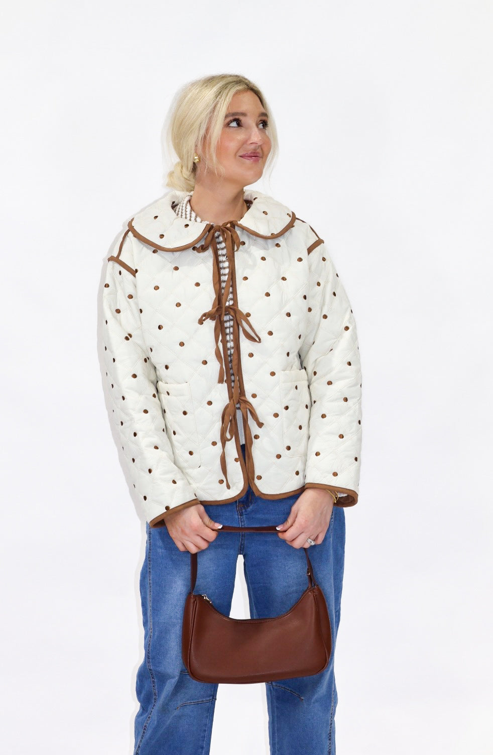 Person wearing a cream-colored jacket with brown accents and holding a brown handbag on a white background