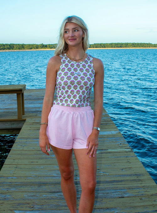 Woman standing on a wooden dock by a lake wearing a patterned top and pink shorts.